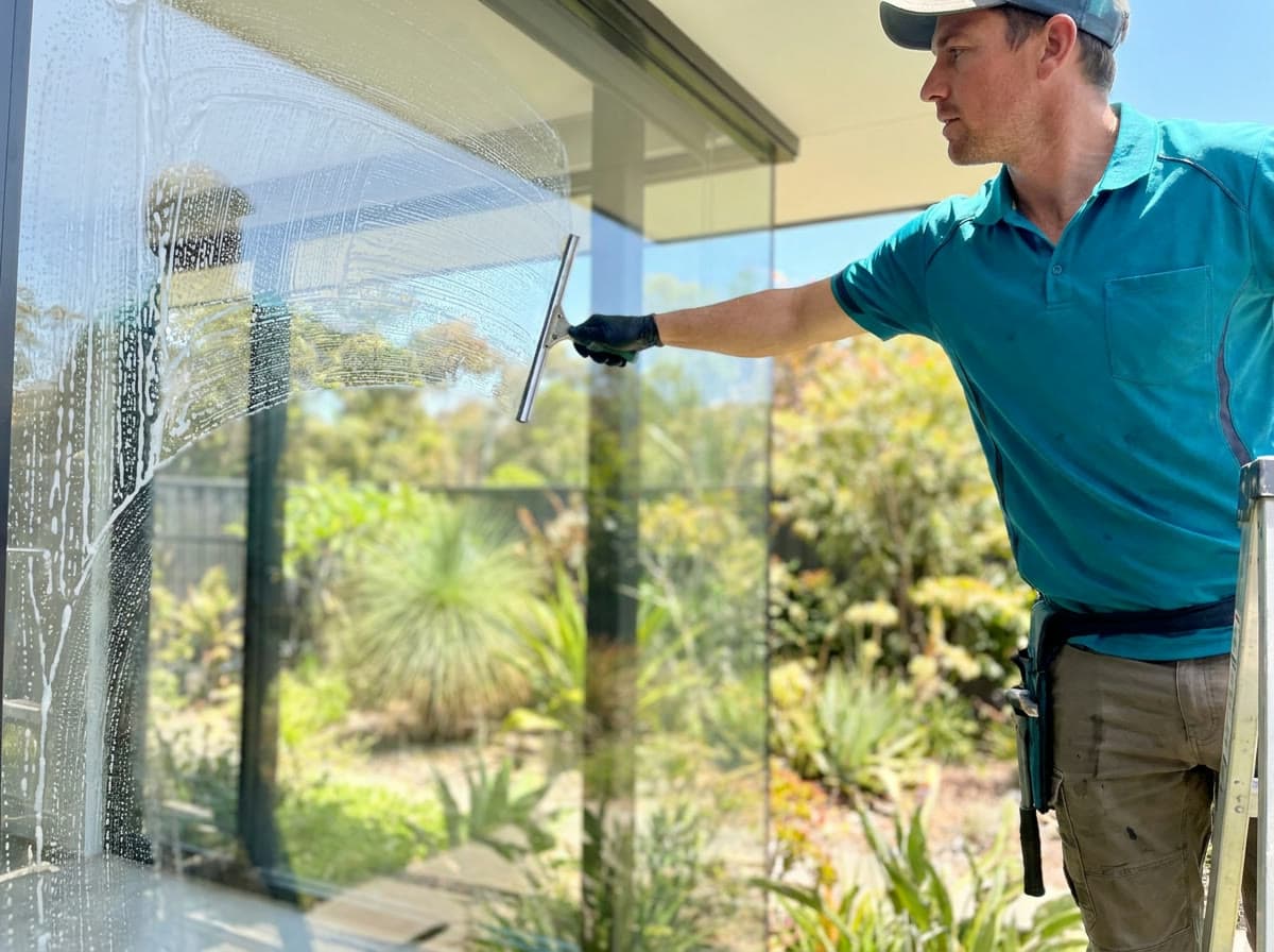 Window cleaner squeegeeing a large window, half soapy and half crystal clear